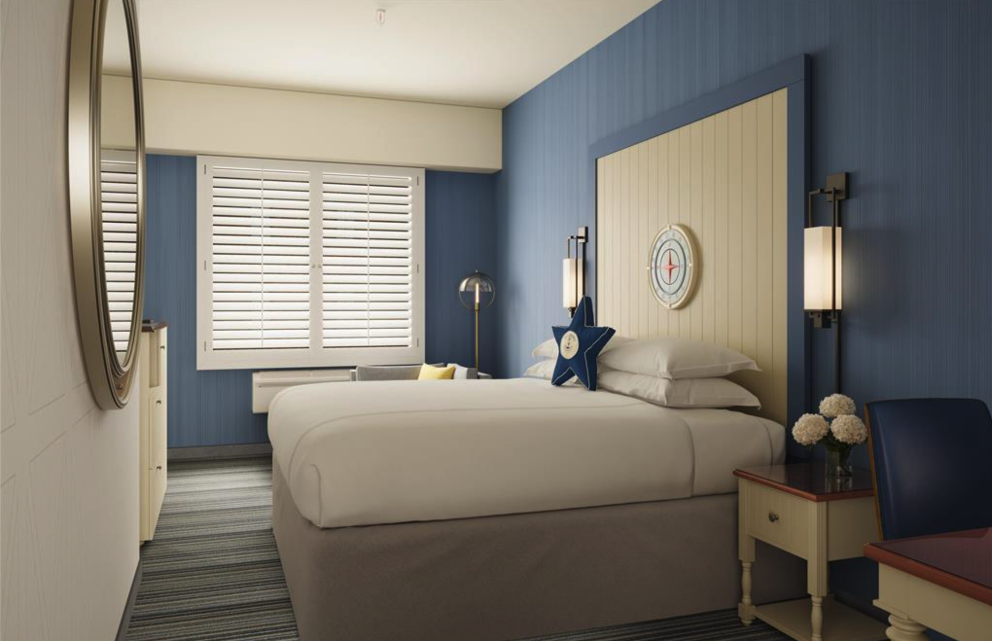 Interior of a bedroom with a bed, blue and cream-colored walls, a window with white blinds, a bedside table with a lamp, a star-shaped pillow, and a bouquet of white flowers on a small table.